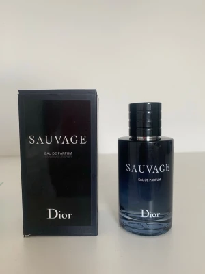 Dior Sauvage Eau de parfum  - Dior Sauvage Eau de Parfum kommer i en elegant mörkblå glasflaska med svart lock och vit text. Förpackningen är svart med tydlig logga och information om att flaskan är påfyllningsbar. En klassisk och stilren doft för dig som gillar exklusiva parfymer.