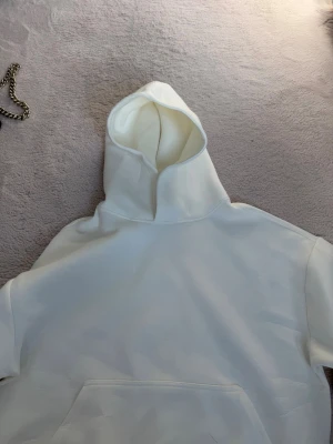Vit hoodie med huva och magficka - Säljer en stilren vit hoodie med klassisk huva och stor magficka framtill. Hoodien har en avslappnad passform och är tillverkad i ett mjukt, tjockt material som känns riktigt skönt mot huden. Perfekt för dig som gillar en clean och enkel look.