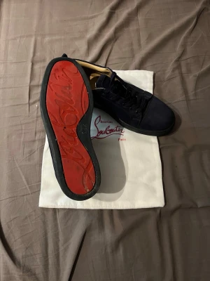 Louboutins - Snygga mörkblå sneakers i mocka från Christian Louboutin med klassisk röd sula och svarta skosnören. Låg modell med stilren design och diskreta detaljer. Perfekta för dig som vill ha något exklusivt och trendigt. Riktigt schysst skick.