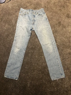 Levis 501 - Ljusblå tvätt på den klassiska straight leg modellen 501. Fint skick och stiliga jeans för dom som gillar att gå för en mer relaxed look. Stilrena detaljer på benen och är i storlek w30. Pris ej hugget i sten 