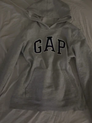 Grå hoodie från GAP - Snygg grå hoodie från GAP med stor logga i svart och vitt på bröstet. 