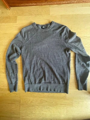 Grå stickad tröja från Uniqlo - Säljer en enkel och stilren grå stickad tröja från Uniqlo. Tröjan har rund halsringning, långa ärmar och ribbade muddar vid ärmslut och nederkant. Perfekt basplagg i garderoben och passar till det mesta.