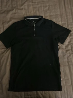 Svart polotopp med dragkedja - Snygg svart polotopp med kort ärm och dragkedja framtill. Perfekt för en stilren look och enkel att matcha med olika outfits. Mjuk och bekväm känsla.