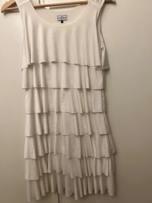 Vit volangklänning från Crocker - Säljer en vit ärmlös klänning från Crocker med flera lager volanger som ger en snygg och lekfull look. Klänningen har rund halsringning och är tillverkad i ett mjukt material som känns skönt mot huden. Perfekt för dig som gillar en feminin stil.