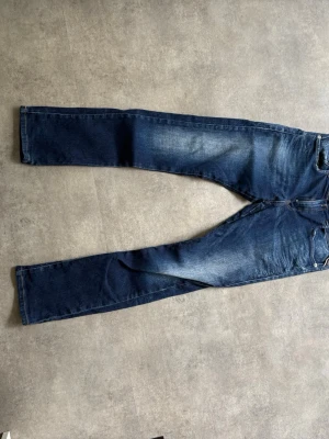 Replay jeans - Säljer ett par mörkblå jeans med raka ben och snygga slitningar på låren och knäna. Jeansen har klassisk femficksdesign och kontrastsömmar. Materialet är denim i bomull. Perfekta för en avslappnad och trendig look.