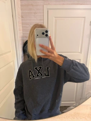 Grå hoodie LXA The Label - Mysig grå hoodie från LXA The Label med stor huva och dragsko. Tryck i svart och vitt framtill. Oversize fit med ribbade muddar vid ärmslut och nederkant. Perfekt för chill dagar eller när du vill ha en avslappnad stil.