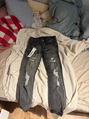 Purple jeans Grå slitna jeans med hål - Säljer ett par purple jean, grå jeans med kraftiga slitningar och hål på båda benen. Jeansen har fem fickor, normal midja och raka ben. Materialet är klassisk denim och de har en cool, trendig look med tvättade detaljer.
