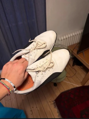 Vita Puma golfskor med svarta detaljer - Säljer ett par vita skor från Puma med svarta detaljer och klassisk snörning. Skorna har låg profil, greppig yttersula och orange innersula. Perfekta för dig som gillar att golfa med en stilren look.