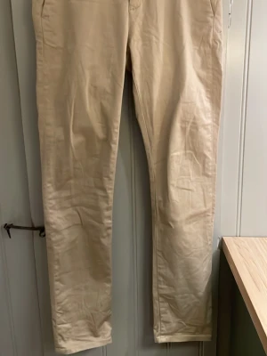 Beiga chinos med rak passform - Snygga beiga chinos med klassisk rak passform och diskreta fickor fram och bak. Perfekta för en clean och stilren look. Tillverkade i mjukt bomullsmaterial som känns bekvämt hela dagen.