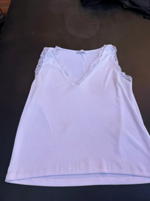 Vit ribbad linnetopp från Zara - Säljer en vit ribbad linnetopp från Zara med spetsdetaljer vid v-ringningen och axlarna. Toppen är ärmlös och har en mjuk, stretchig känsla som passar perfekt till sommaren. Enkel men ändå söt design som är lätt att matcha.