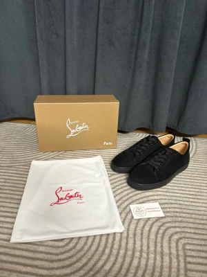Svarta sneakers från Christian Louboutin - Stilrena svarta sneakers från Christian Louboutin i mocka med klassisk låg profil och ikoniska röda sulor. Skorna har svarta skosnören och diskret design som passar till många olika outfits. Kommer med originalkartong och dustbag.