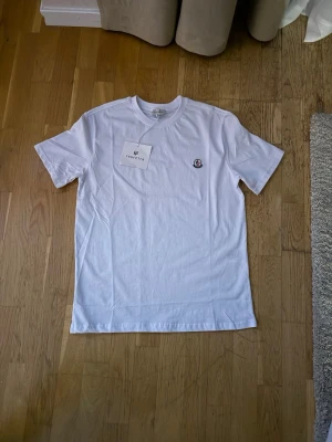 Vit t-shirt från Moncler - ÄKTA !Säljer en klassisk vit t-shirt från Moncler med rund hals och diskret logga broderad på bröstet. Tillverkad i mjuk bomull och har en clean, enkel design som passar till allt.