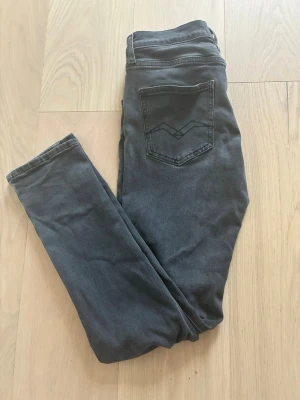 Replay Jeans mörkgråa 158 - Snygga mörkgrå slim fit jeans med klassisk femficksdesign och raka ben. Jeansen har en diskret bakficka med dekorativ söm och en liten patch bak i midjan. Perfekta för dig som gillar en enkel men stilren look.