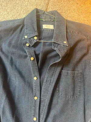 Mörkblå skjorta från Eton - Nypris ca 1800kr. Säljer en klassisk mörkblå skjorta från Eton i mjuk bomull. Skjortan har knappar hela vägen, bröstficka och button-down krage. Perfekt för dig som gillar stilrena och tidlösa plagg.