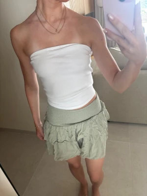 Ljusgrön kjol med volang - Säljer ett par ljusgrön kjol med bred, ribbad midjeresår och volangdetaljer. De har en luftig och flowy passform som gör dem perfekta för varma sommardagar. Styla med en enkel topp för en chill look.