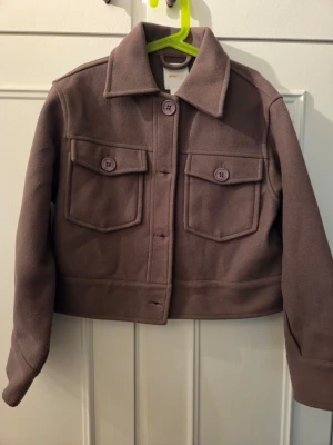 Ljusbrun  jacka med fickor - Snygg ljusbrun jacka/overshirt i mjukt tyg med två stora bröstfickor och knappar framtill. Jackan har en rak, boxig passform och klassisk krage. Perfekt att slänga över en hoodie eller t-shirt för en chill look.