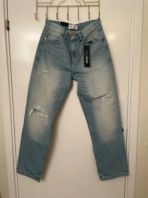 Baggy ljusblå jeans med slitningar, 31W / 32L nya  - Baggy jeans i ljusblå tvätt med slitna detaljer på benen och klassisk femficksdesign. Jeansen har hög midja och raka ben för en avslappnad look. Perfekta för dig som gillar en trendig och bekväm stil. Stl 31W / 32L nya 