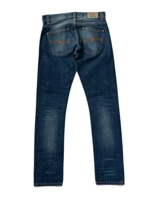 Nudie Grim Tim selvedge-jeans. - Snygga blå jeans med raka ben och slitna detaljer framtill. Jeansen har klassiska fem fickor och kontrastsömmar, samt en patch bak i midjan. Materialet är denim i bomull med en tvättad look och markerade slitningar för en avslappnad stil.