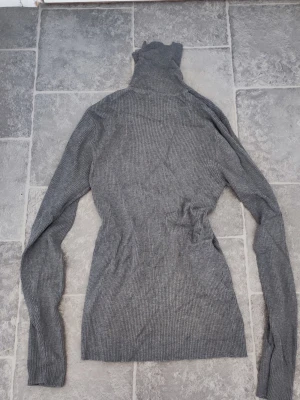 Grå polotröja från Gina Tricot - Säljer en ribbstickad grå polotröja från Gina Tricot i storlek XL. Tröjan har lång ärm, hög polokrage och är tillverkad i mjukt, stretchigt material. Perfekt för lager på lager och enkel att matcha med olika outfits.