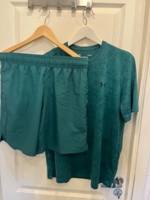 Turkos träningsset från Under Armour - Säljer ett matchande träningsset från Under Armour i turkos färg. Setet består av en t-shirt med rund hals och korta ärmar samt ett par shorts med resår i midjan och vit sidopanel. Perfekt för gymmet eller löprundan.