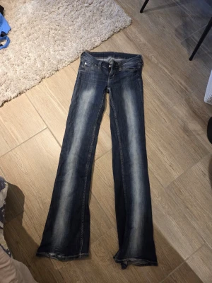 Mörkblå bootcut jeans med slitningar - Snygga mörkblå bootcut jeans med slitningar längs benen och klassisk femficksmodell. Jeansen har en låg midja och ljusare tvättade partier framtill och baktill för en cool, avslappnad look. Tillverkade i denim med en skön passform. De har dock sprukit i märket där bak men det är ingenting som gör jeansen oanvänd bara. Tycker själv att de ger en kolare look.