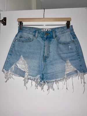 Ljusblåa högmidjade jeansshorts - Säljer ett par ljusblåa högmidjade jeansshorts med slitna detaljer och fransig kant. — Shortsen har klassisk femficksdesign och råa hål framtill för en edgy look. — Perfekta för sommaren och riktigt snygga till sneakers eller sandaler. — Sparsamt använda, i mycket bra skick. — Inköpta på Carlings i märket Stay. — Nypris ca. 500 kr.