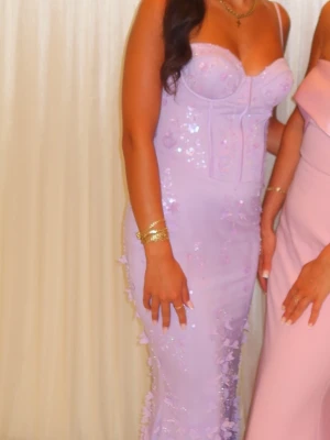 Ljuslila Oh Polly klänning med paljetter  - Säljer en elegant ljuslila långklänning med smala axelband och v-ringad byst. Klänningen är dekorerad med paljetter och 3D-blommor längs hela kjolen för en extra glamorös look. Perfekt för bal eller festliga tillfällen. Pris kan diskuteras