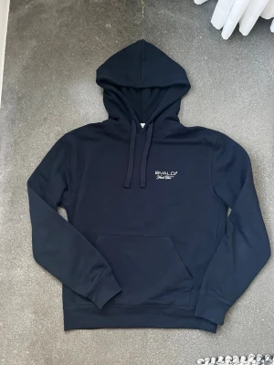 Svart hoodie från BVALDI med tryck - Svart hoodie från BVALDI med huva och dragsnören. På bröstet finns en liten logga och på ryggen ett stort tryck med en båt och BVALDI-text. Klassisk känguruficka framtill och ribbade muddar. Perfekt för en chill och stilren look. Hoodien har alldrig används så är i nyskick! Är i storlek 170 men skulle säga att den också passar som XS. Priset går absolut att diskuteras!