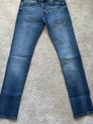 Blå slim fit jeans med klassisk tvätt - Säljer ett par blå slim fit jeans med klassisk tvätt och fem fickor. Jeansen har en något urtvättad look framtill och baktill, samt raka ben. Perfekta för en avslappnad och stilren outfit.
