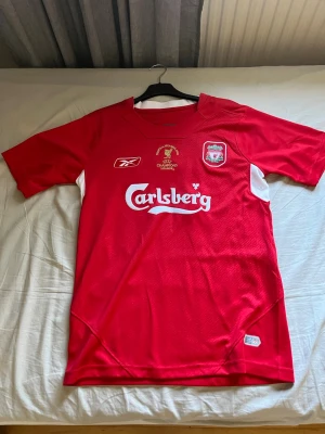Liverpool matchtröja Gerrard #8 - Säljer en röd Liverpool tröja från 2005 med Steven Gerrard på ryggen med cl badge. Köpt på fotbollsmarknaden. Ny pris 549. Storlek s men kommer passa om man har xs också. Säljer då den är för liten. Kan gå ner i pris vid snabb affär. Aldrig använd 