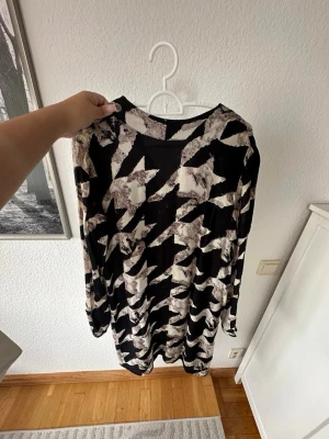 Svart och vit mönstrad långärmad klänning - Säljer en svart och vit långärmad klänning med ett coolt abstrakt mönster. Klänningen har en avslappnad passform och är tillverkad i ett mjukt material som känns skönt mot huden. Perfekt för dig som gillar statement-plagg med unik design.