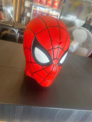 Spiderman huvud- dekoration  - Ett dekorativt Spiderman huvud i röd plast med svarta spindelnätslinjer och stora vita ögon. Huvudet har en rundad form och är detaljerat målat för att efterlikna Marvels superhjälte. Perfekt som samlarpryl eller cool dekoration. Kan användas som popcorn huvud med 
