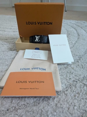  lv svart läderarmband - Snyggt svart armband i äkta läder med ikoniskt monogram och silverfärgad lv detalj framtill. Armbandet har klassisk design och levereras med original ask och dustbag. Perfekt accessoar för dig som gillar exklusiv stil.