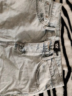 Ljusblå jeanskjol från 157 - Snygg ljusblå jeanskjol från 157 med klassisk femficksdesign och bälteshällor. Kjolen har en rak passform och är perfekt för dig som gillar en avslappnad och trendig stil. Modellen heter MADDY. Passar som s-m