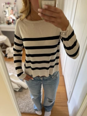 Randig långärmad tröja från Zara - Snygg långärmad tröja från Zara i beige med svarta horisontella ränder. Tröjan har en rund halsringning och är tillverkad i ett tunt, mjukt material som känns skönt mot huden. Perfekt för en avslappnad och trendig look.