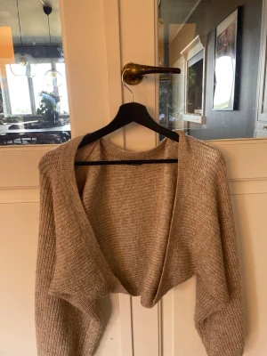 Beige stickad bolero Gina Tricot - Kort beige stickad bolero från Gina Tricot i mjukt material. Modellen har öppen front och långa ärmar med ribbstickad struktur. Perfekt att slänga över en topp för extra värme och stil.