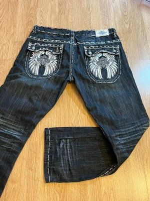 KDNK Kayden.K Y2K Embroidered Baggy Jeans W40 L32 Streetwear - Rare KDNK (Kayden.K) premium denim jeans featuring oversized embroidered back pockets, rhinestone and stud detailing, contrast white stitching, and a dark wash. Classic Y2K streetwear design with a relaxed baggy fit and heavyweight 100% cotton denim.Very good used condition. A few small studs are missing, but it is barely noticeable and does not affect the overall look of the jeans.      Approx. laid flat: • Waist: 50 cm • Total length: 113 cm