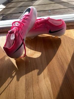 Nike rosa fotbollsskor med dobbar - Säljer ett par snygga fotbollsskor från Nike i rosa och vitt med svarta detaljer. Skorna har klassisk snörning, låg profil och dobbar för bra grepp på planen. Ovandelen är i syntetmaterial och sulan har en glansig finish. Perfekta för dig som vill sticka ut på matchen! Strl är 41, fast känns som 43. Pris kan diskuteras!!!