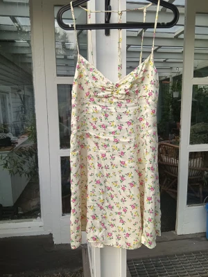 Kort blommig sommarklänning  - Säljer en snygg, lätt sommarklänning från Zara med unik design i nyskick. Ryggen är bar från midjan och uppåt med knyt bara tunna axelband. Det är en kort klänning i siden/silke som är stum i passformen.