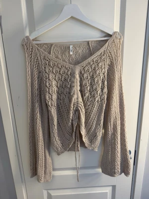 Beige virkad tröja med v-ringning - Säljer en beige stickad tröja från Monki med v-ringning och snörning framtill. Tröjan har ett virkat mönster, vida ärmar och är gjord i ett lätt material som passar perfekt till lager på lager. Superfin detalj med snörningen framtill!