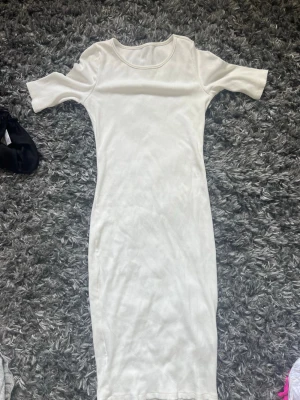 Vit ribbad midiklänning - Säljer en enkel och stilren vit ribbad klänning med korta ärmar och rund hals. Klänningen har en kroppsnära passform och är perfekt för en clean och fräsch look. Materialet känns mjukt och stretchigt.
