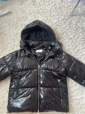 Svart glansig pufferjacka Ivyrevel - Höstjacka orginalpris är 799kr. Säljer en svart glansig pufferjacka från Ivyrevel med huva och dragkedja framtill. Jackan har två sidofickor och breda kanaler för extra värme. Materialet är syntet med en riktigt snygg shiny finish som sticker ut. Perfekt för kalla vinterdagar.
