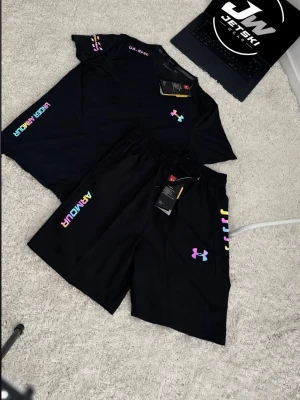 Under armour set sommaren  - Snyggt svart träningsset med t-shirt och shorts från Under Armour. Båda plaggen har färgglada loggor och textdetaljer i regnbågsfärger. Perfekt för gymmet eller sportaktiviteter. Materialet är lätt och andas bra.