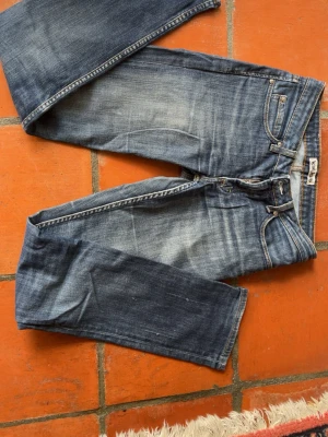 Blå Acne Jeans med dragkedja - Ett par vintage jeans från 2004-2008. Modell: ”HEP”. Jeansen har en snygg tvättad look med slitningar och kontrastsömmar. Perfekta till vardags för en avslappnad stil.