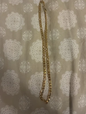 Kedjehalsband i guldton - Snyggt halsband med breda, platta länkar i guldton. Kedjan har en klassisk design som passar perfekt till olika stilar och är enkel att matcha med andra accessoarer. Materialet ger ett lyxigt intryck och länkarna är rejäla för en trendig look.
