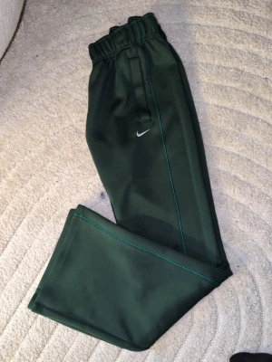 Mörkgrön  Nike dress  helt ny dam - Mörkgrön Nike dress  från Nike med rak passform och resår i midjan. Byxorna har en liten vit Nike-logga på vänster lår och är tillverkade i ett mjukt och bekvämt material, perfekt för chill dagar. Matchar snyggt med en hoodie eller ziptröja. Helt ny tjej dress storlek S  pris på tröja 849kr mjukis 799kr 1600 cirka tillsammans  säljes för 1100 .endast testade hemma 