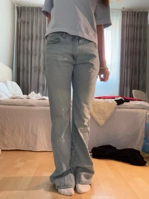 Ljusblå raka jeans - Säljer ett par ljusblå jeans med rak passform. Jeansen har klassiska fem fickor och en avslappnad look. Materialet är denim i bomull och benen är långa med lätt utsvängd siluett. Perfekta för en casual och trendig stil. Längst ner på benet finns lite slitage.