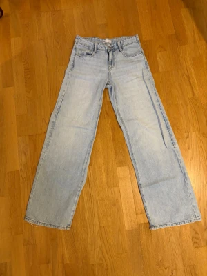 Ljusblå raka jeans med hög midja - Säljer ett par ljusblå baggy jeans och låg midja. Jeansen har klassisk femficksdesign och råa kanter vid bensluten för en avslappnad look. Perfekta till sneakers eller boots och passar till många olika stilar.