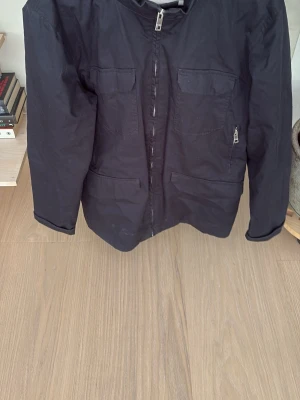 Mörklbå jacka - Stilren mörklblå vindjacka med fyra fickor framtill och hel dragkedja. Perfekt för dig som vill ha en clean look och praktiska detaljer.