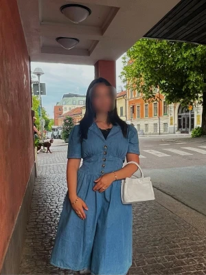Blå jeansklänning med knappar - Snygg blå jeansklänning med korta ärmar och knappar framtill. Klänningen har en markerad midja och v-ringad hals. Perfekt för dig som gillar en avslappnad men ändå stilren look.